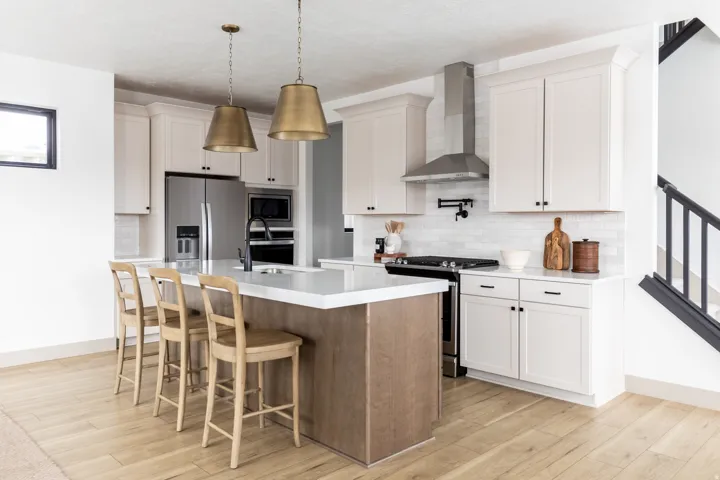 Two tone kitchen with stainless steel appliances, a kitchen bar, light wood finished floors, an island with sink, and two tone cabinets