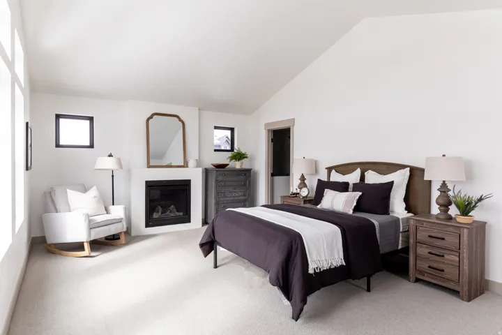 Bedroom with a glass covered fireplace, lofted ceiling, and light carpet