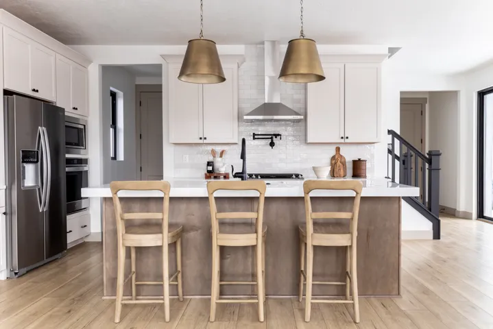 Kitchen featuring stainless steel appliances, a kitchen island with sink, white cabinets, decorative light fixtures, and light wood-style flooring