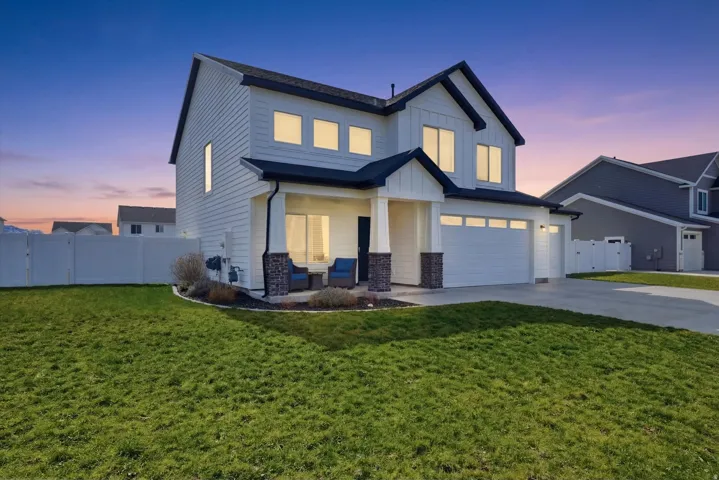 View of front facade with an attached garage, a gate, driveway, board and batten siding, and stone siding