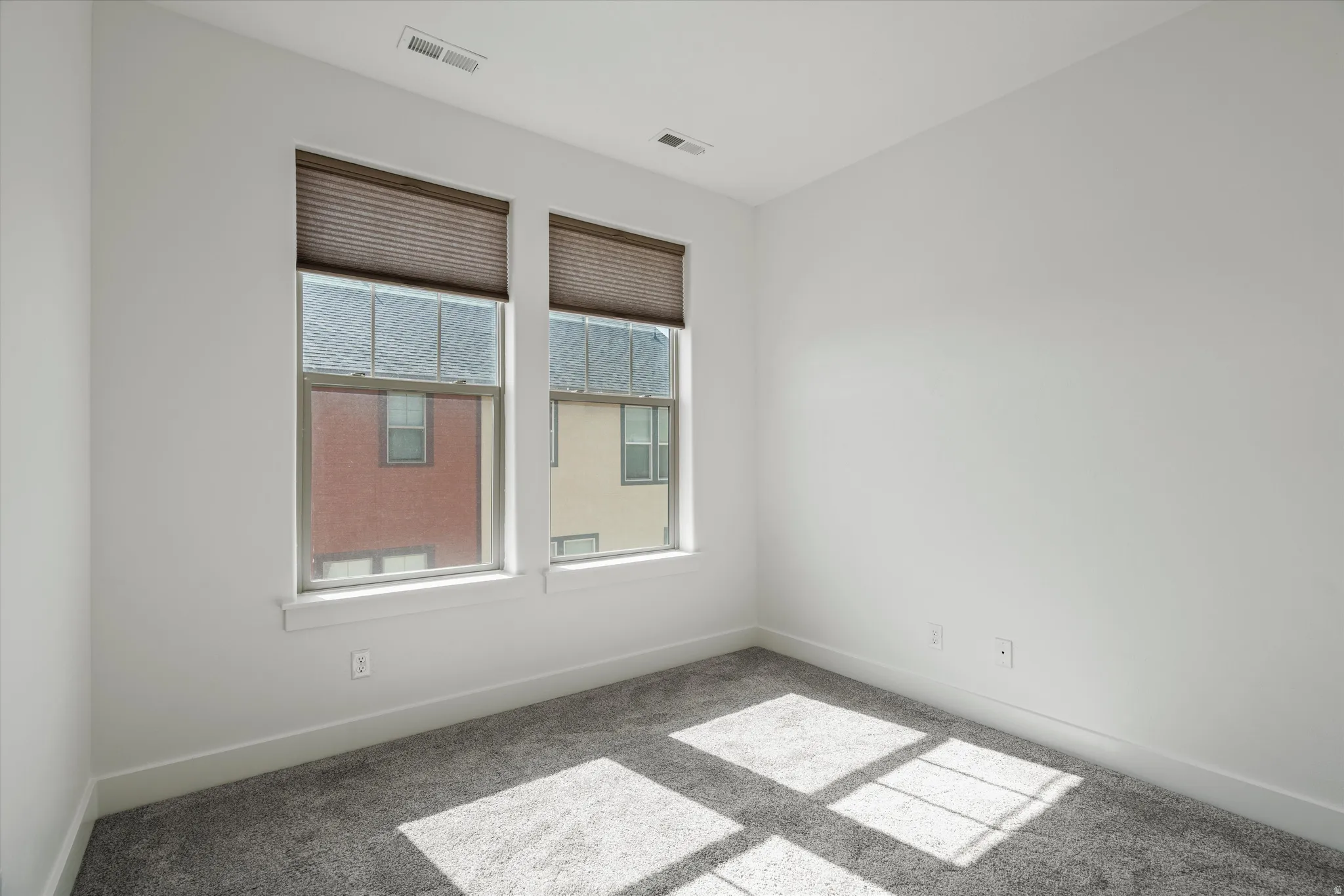 Bright interior space featuring two windows with privacy blinds, plush grey carpeting, white baseboards, and neutral wall finishes