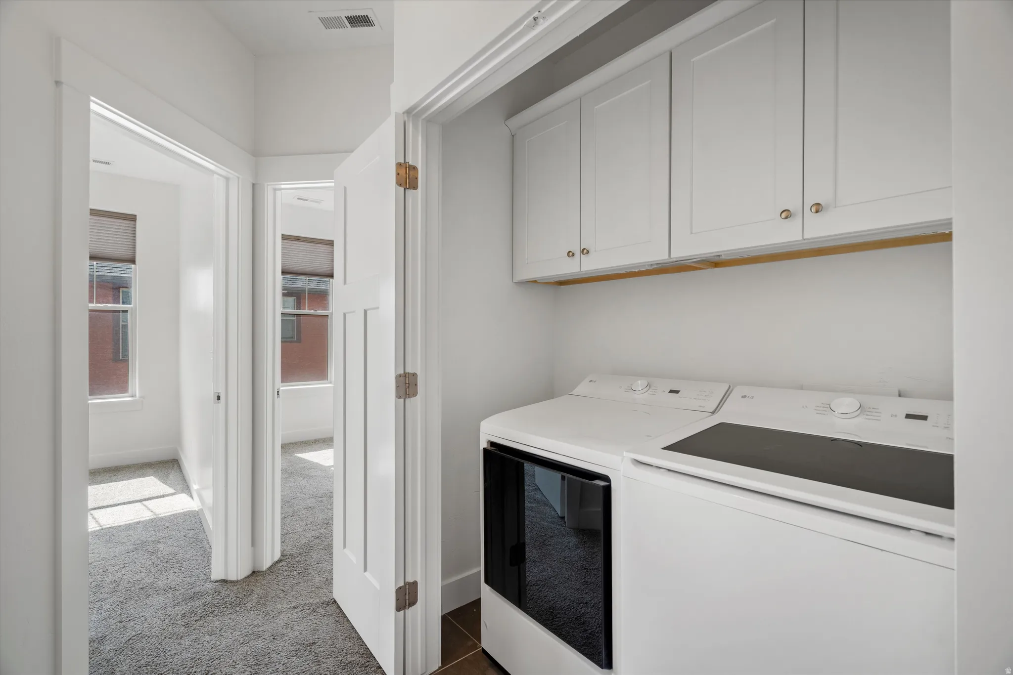Integrated laundry area featuring white cabinetry with gold-tone hardware and a tiled floor