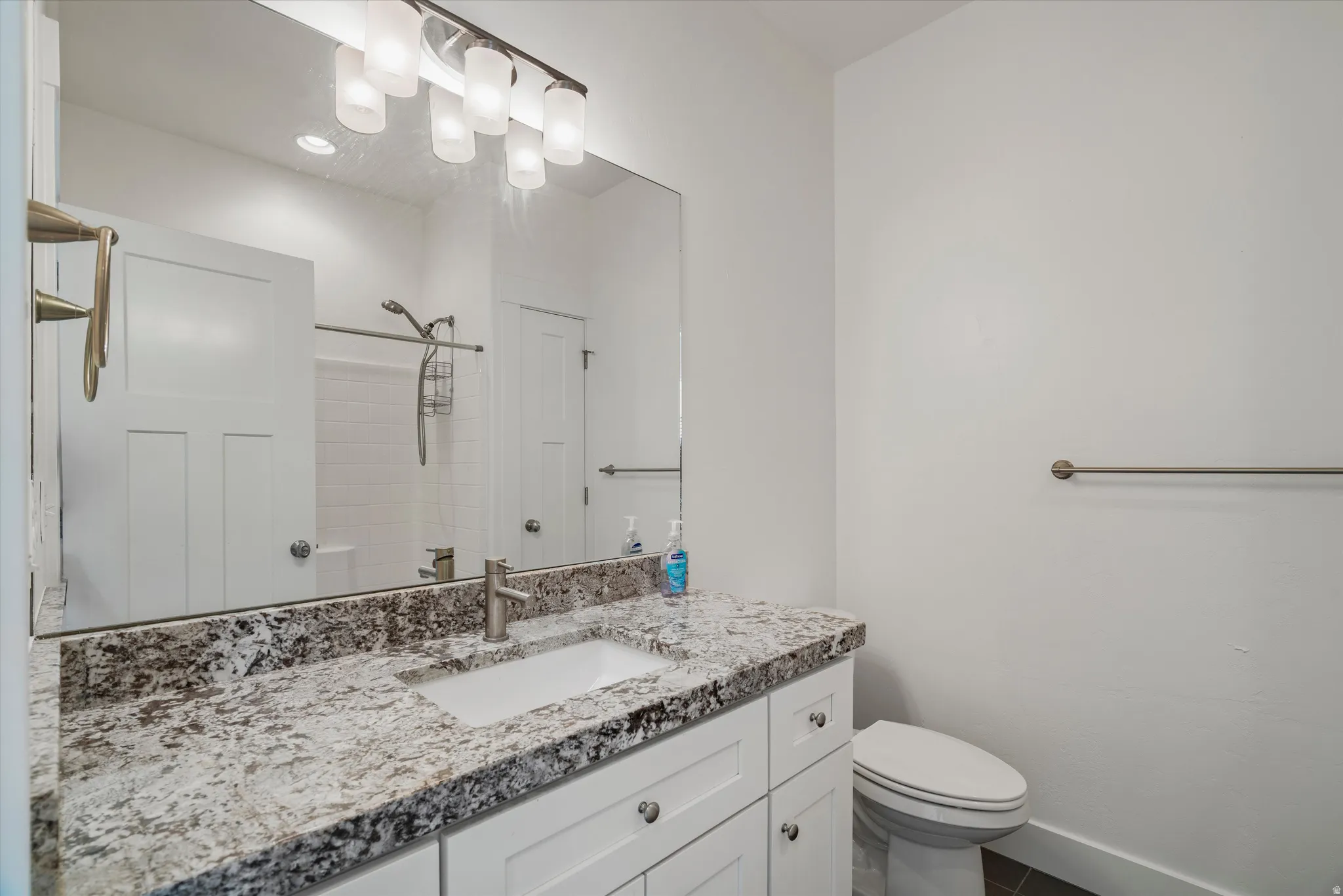 Bathroom featuring a vanity with a light-toned, speckled countertop, an undermount sink, and white cabinetry with brushed nickel hardware