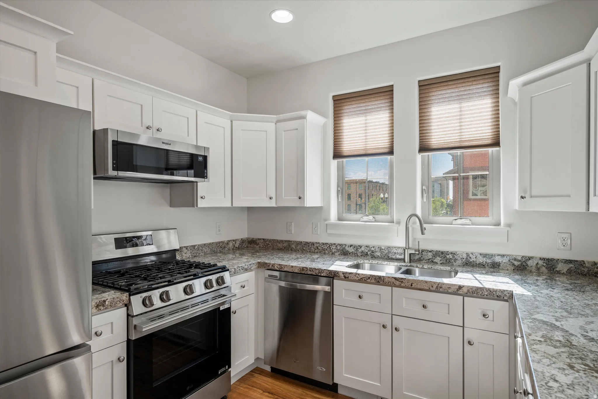 Kitchen featuring white shaker-style cabinetry, stainless steel appliances, granite-style countertops, and a double basin sink