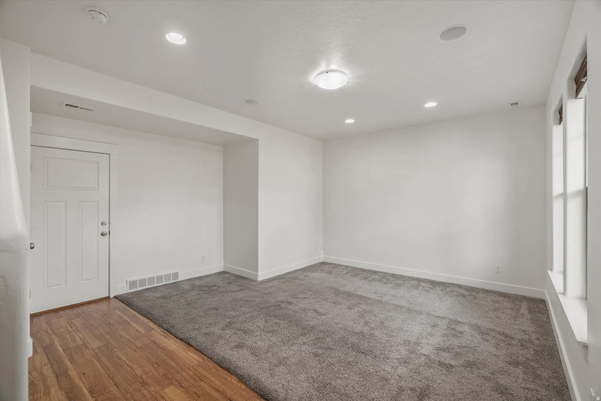 Neutral white walls in a versatile room featuring recessed lighting, a ceiling-mounted light fixture, and a window with a white sill
