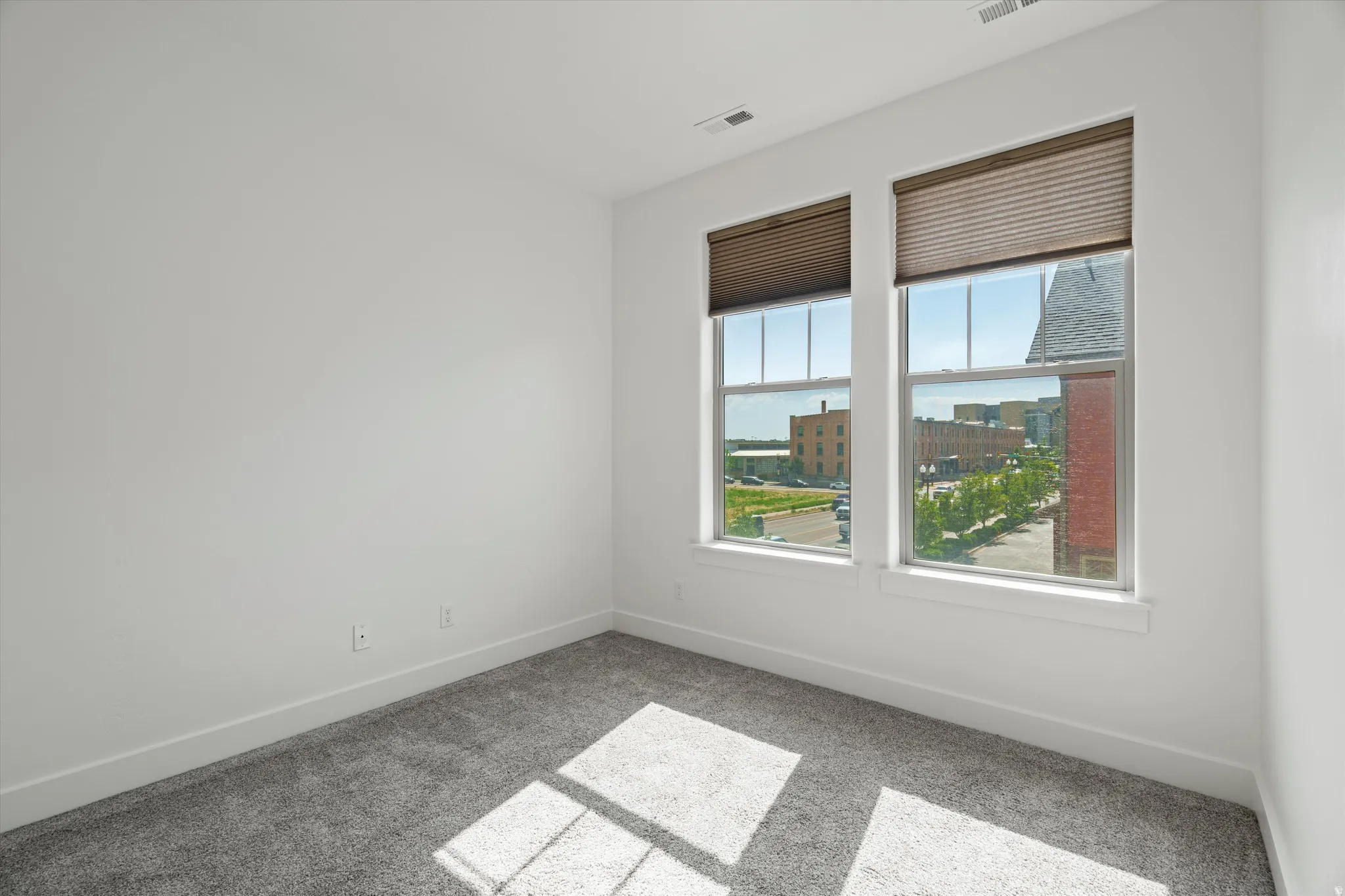 Room featuring two large windows with horizontal blinds, neutral-toned carpet flooring, white walls, and white baseboards