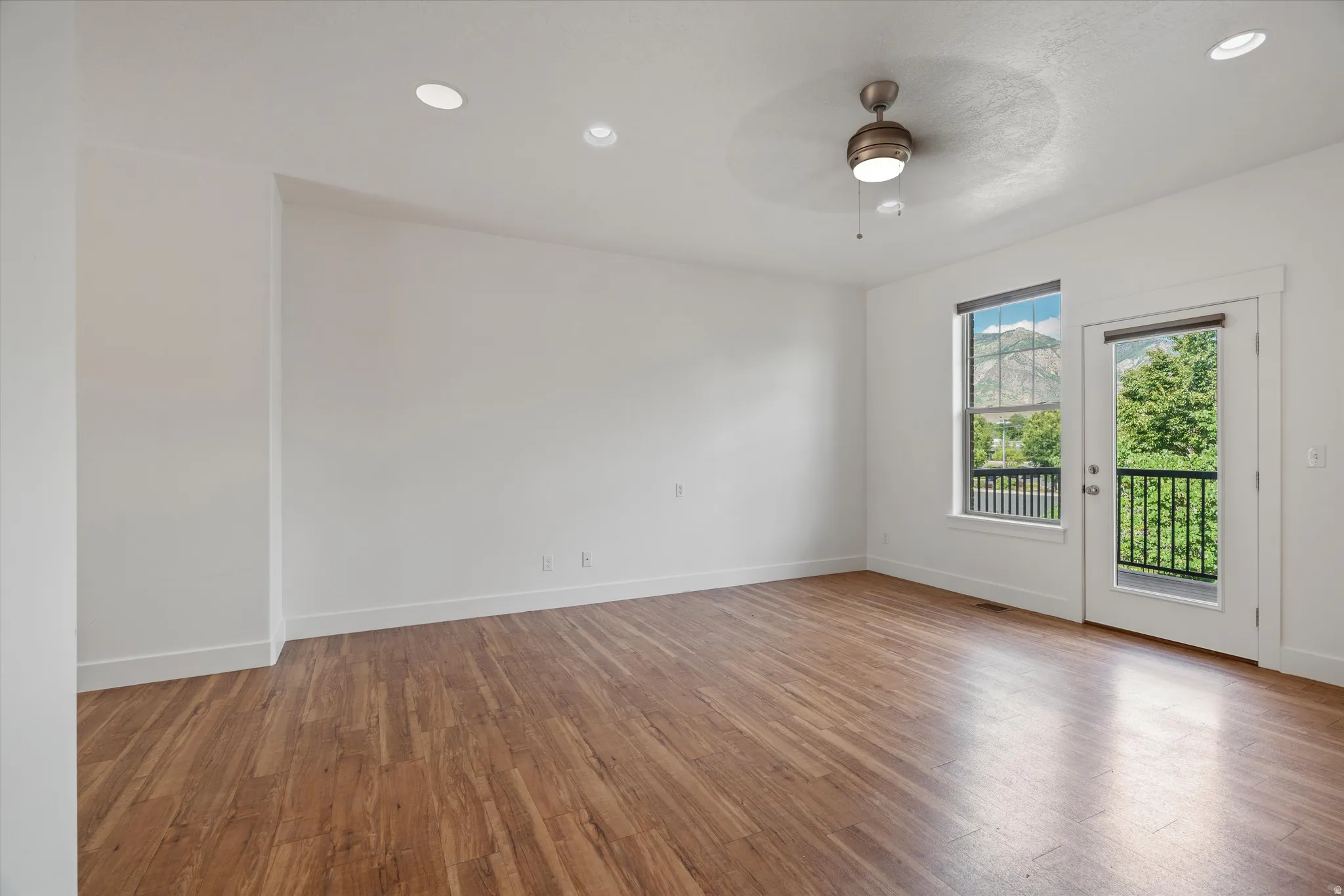 Spacious room featuring wood-finish flooring, recessed ceiling lighting, and a ceiling fan