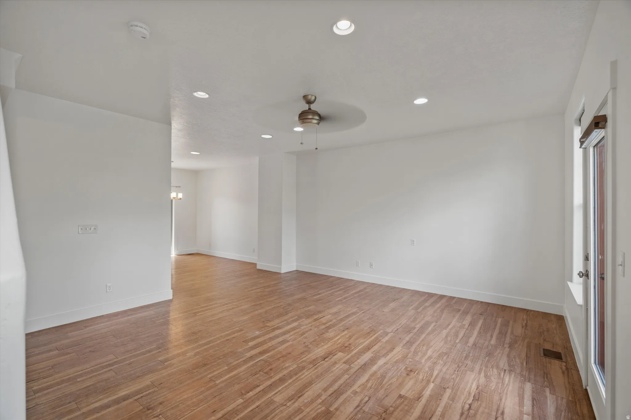 Spacious room featuring wood-finish flooring, recessed lighting, a ceiling fan with an ornamental medallion, white walls, and a glass-paneled door