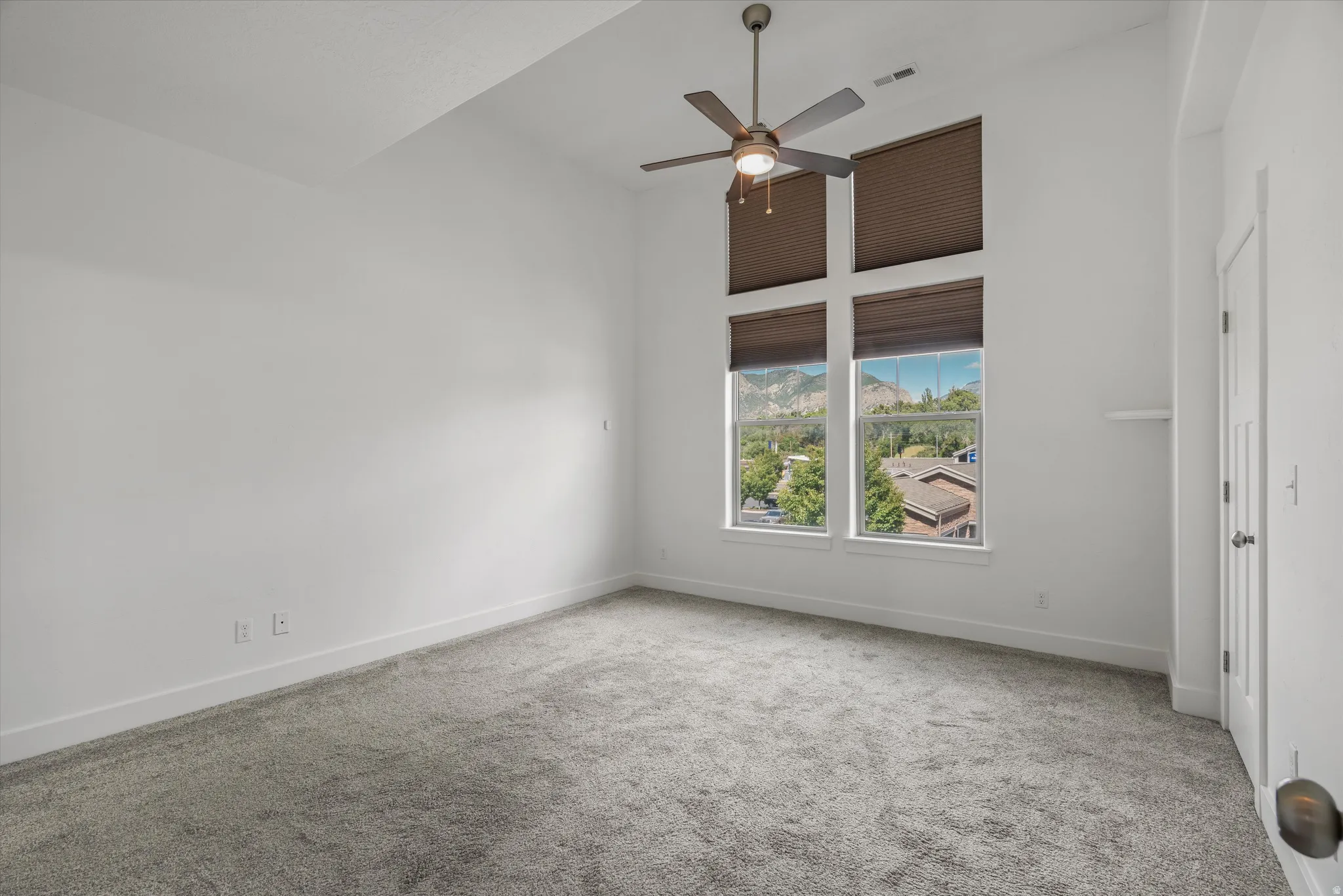 Room featuring high vaulted ceilings, large windows with mountain and tree scenery, a ceiling fan, and grey carpet flooring