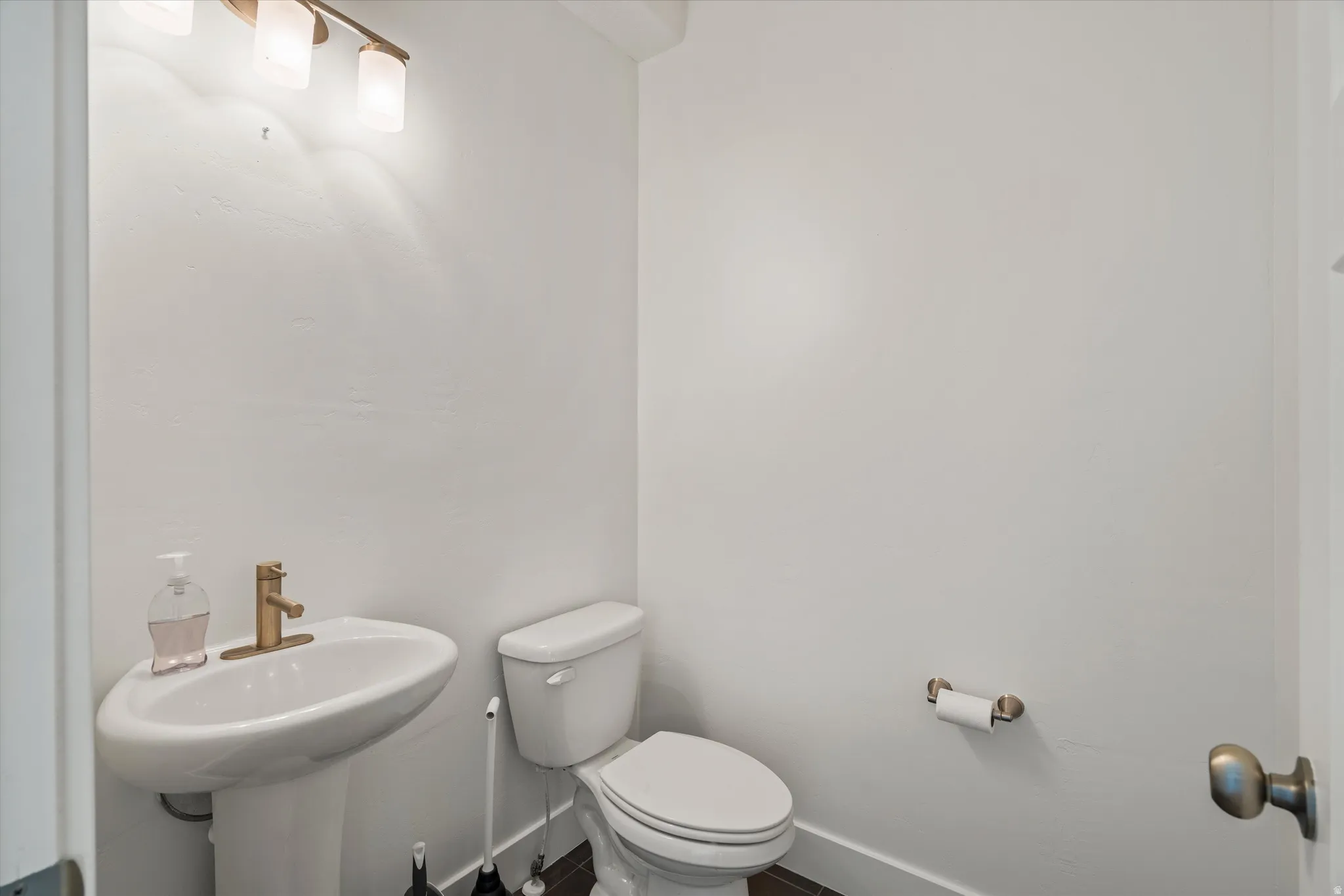 Modern bathroom featuring a pedestal sink, white toilet, and dark wood-finish flooring
