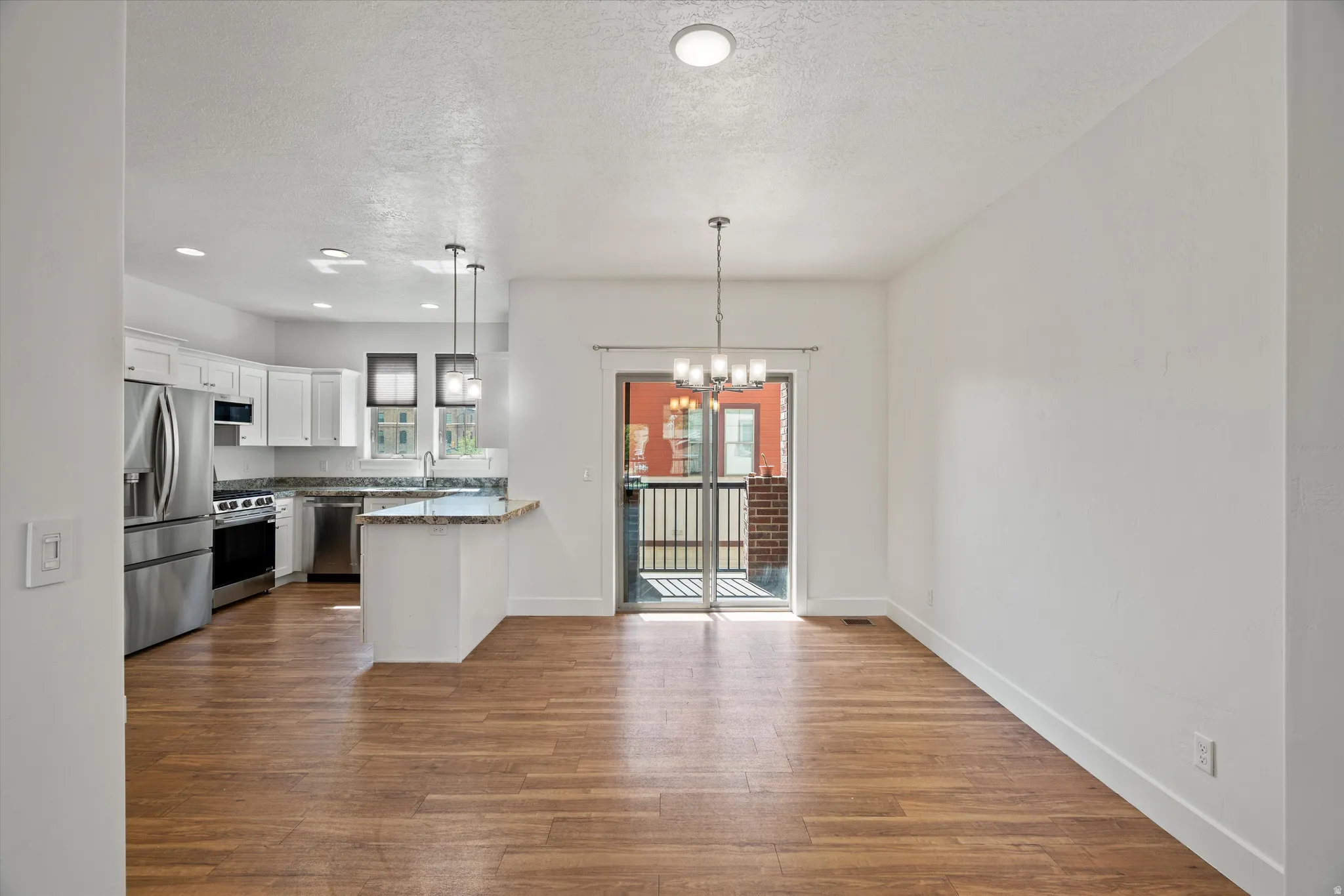 Open-concept living area featuring wood-finish flooring, a contemporary chandelier, and sliding glass doors leading to an exterior balcony