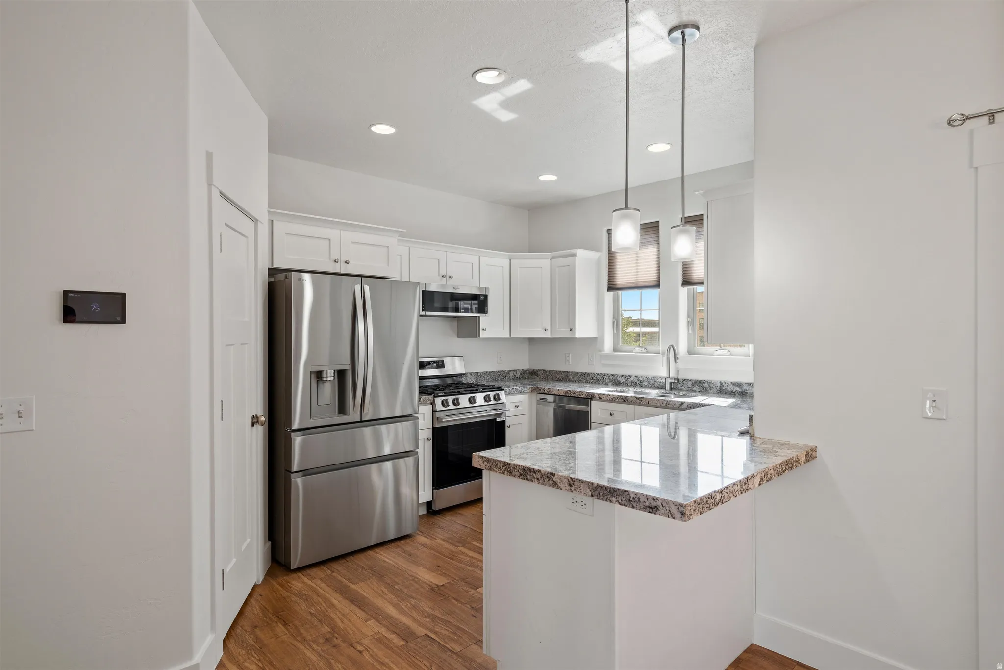 Contemporary kitchen featuring white cabinetry, stainless steel appliances, granite countertops, and wood-finish flooring