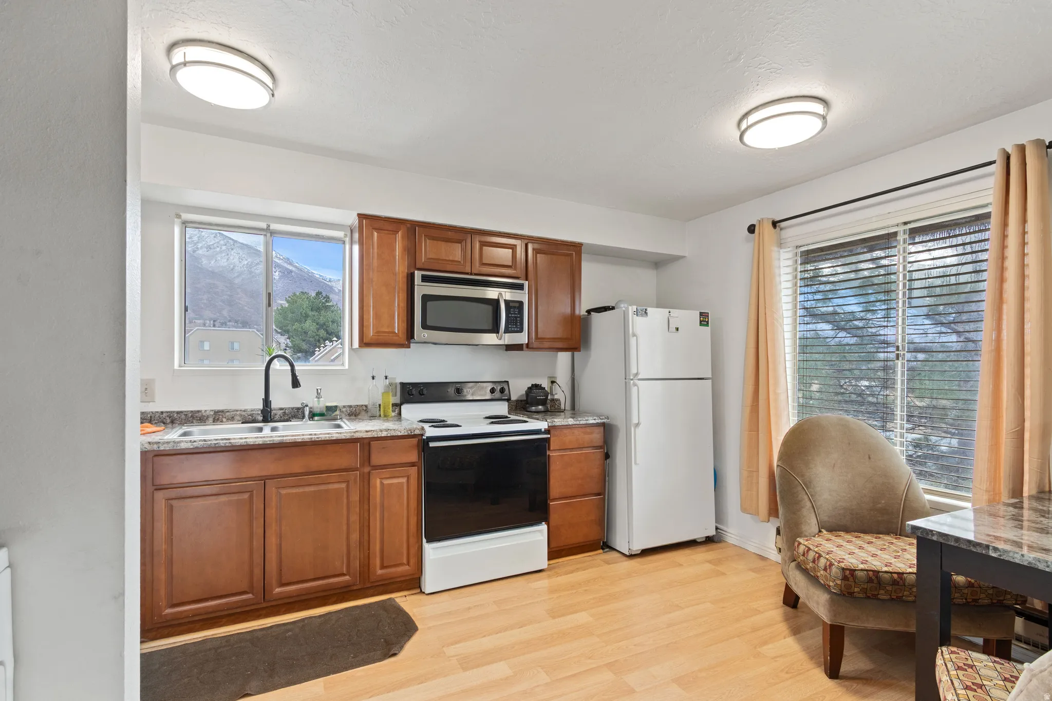 Kitchen featuring white appliances, wood finish cabinets, light wood-style floors, and light stone countertops