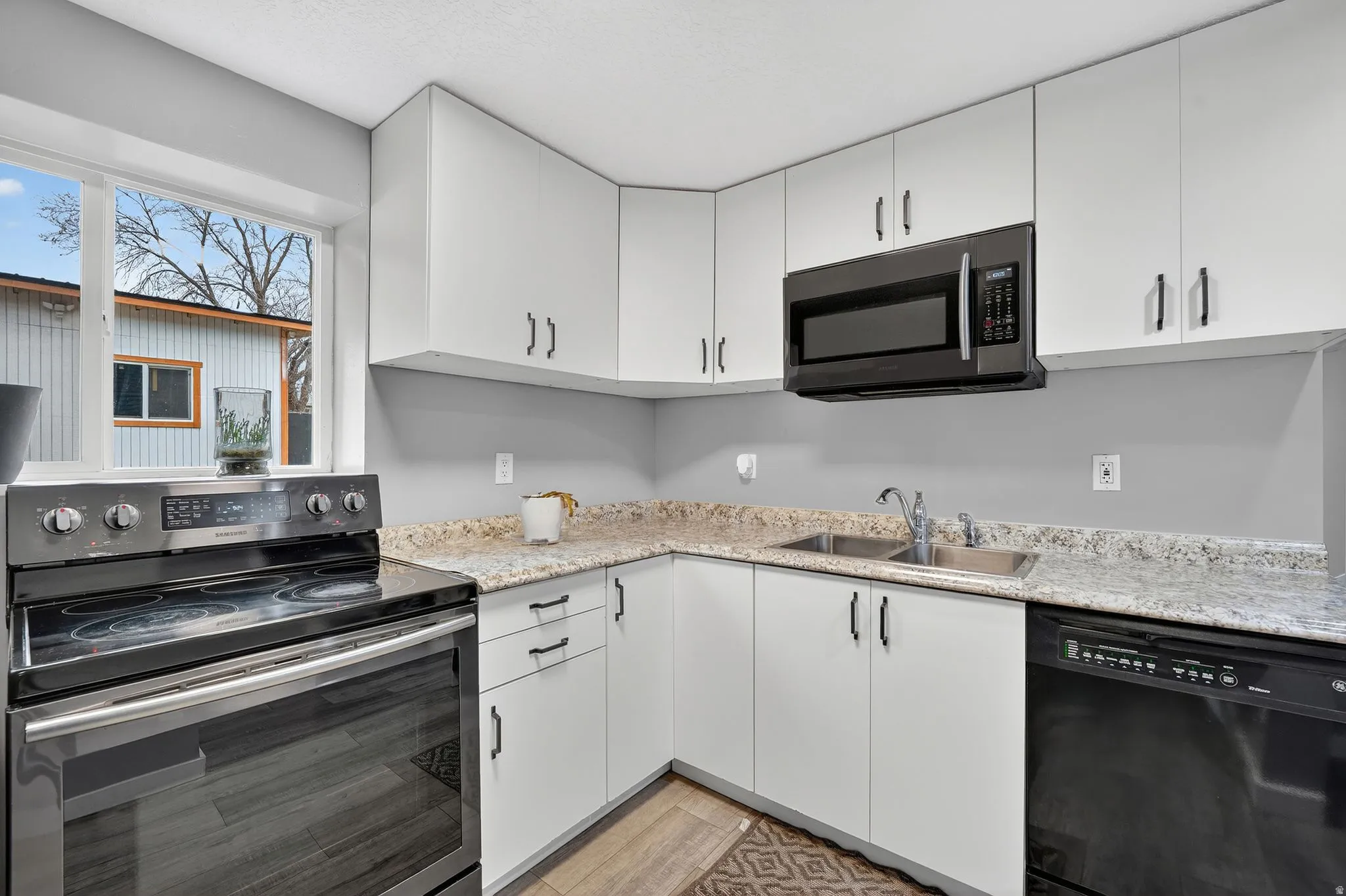 Kitchen with stainless steel appliances, white cabinets, light wood finished floors, and light stone counters