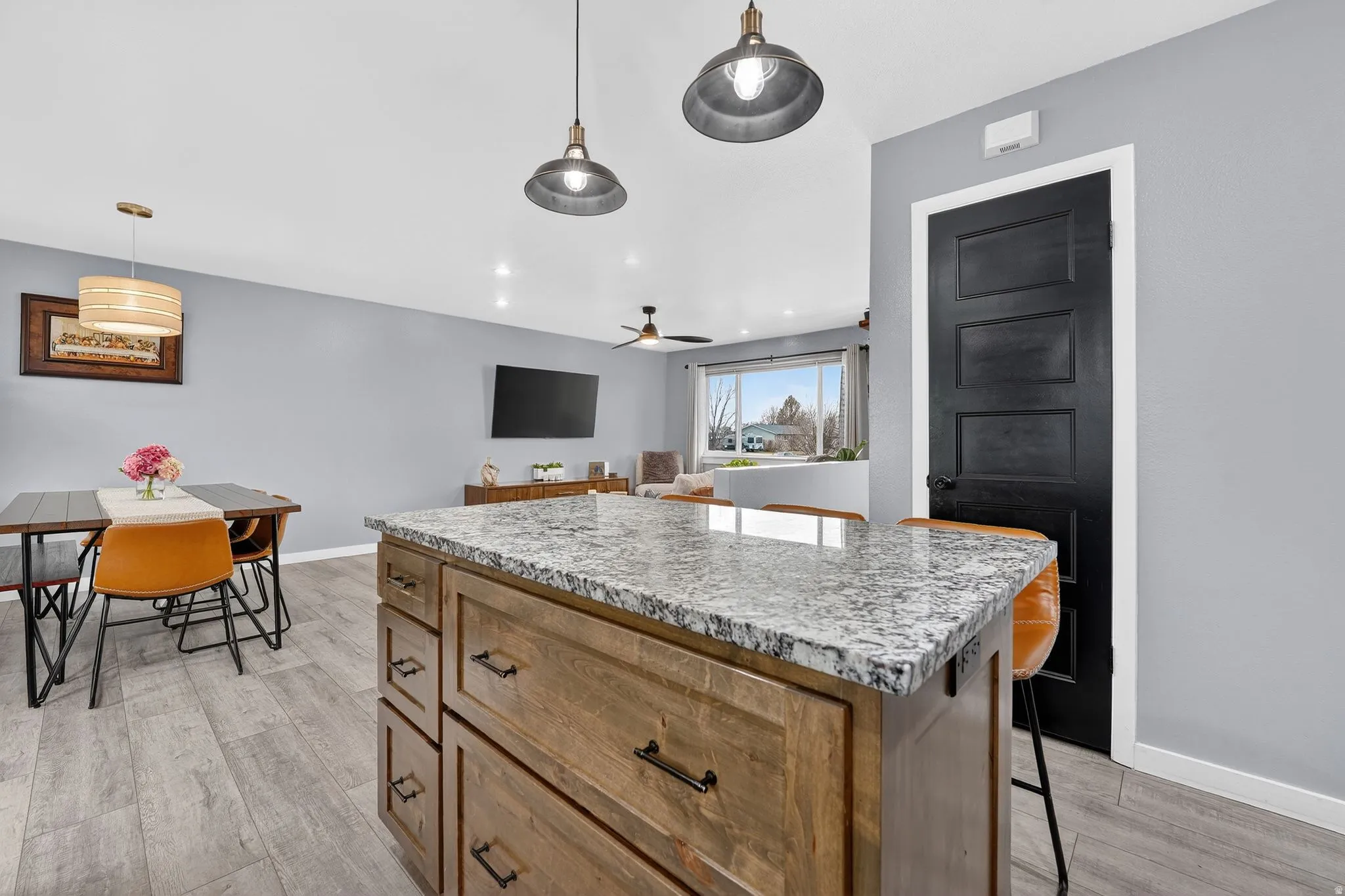 Kitchen with a kitchen island, light stone countertops, a breakfast bar, light wood finished floors, and hanging light fixtures