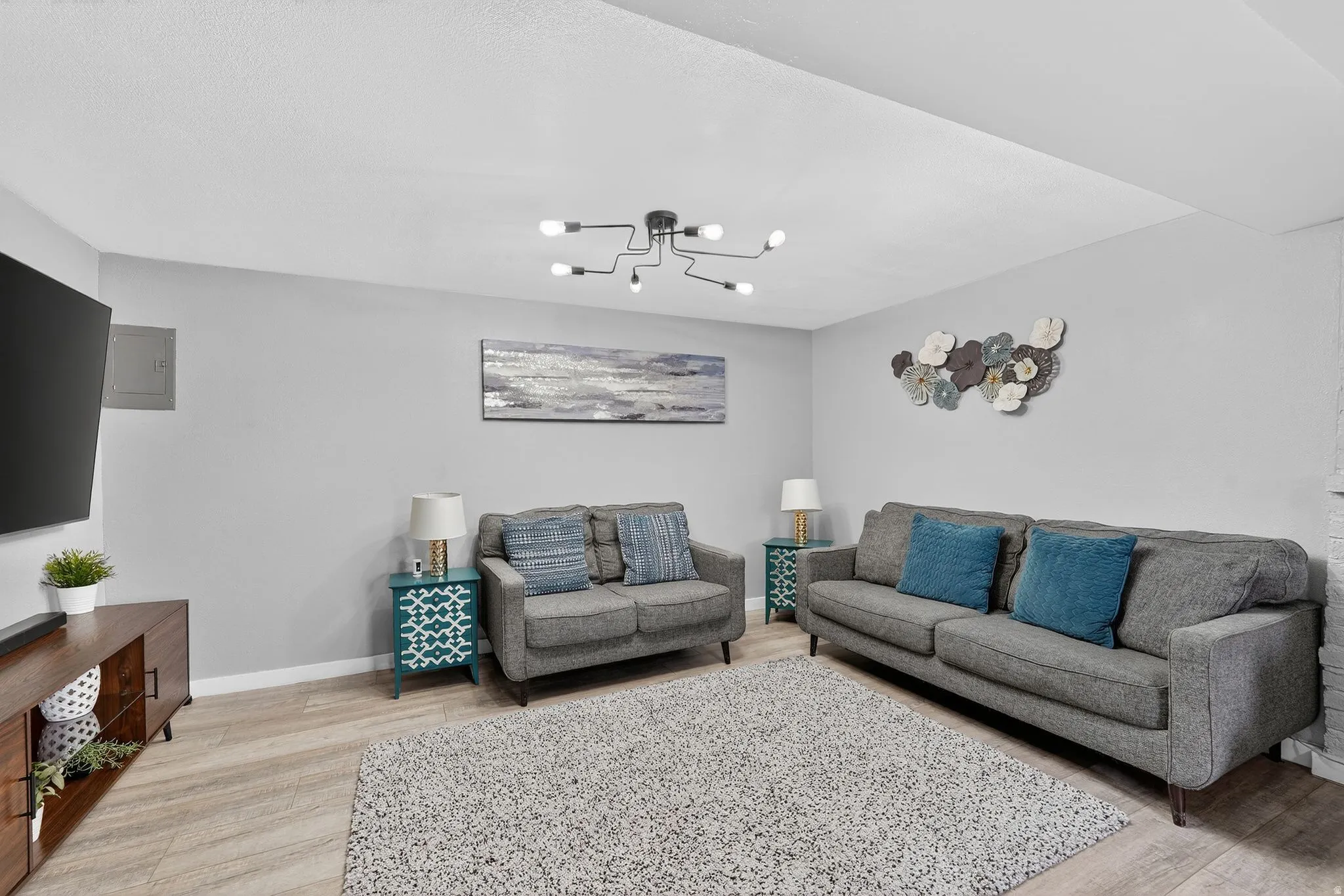 Living area featuring light wood-type flooring, electric panel, and suspended lighting