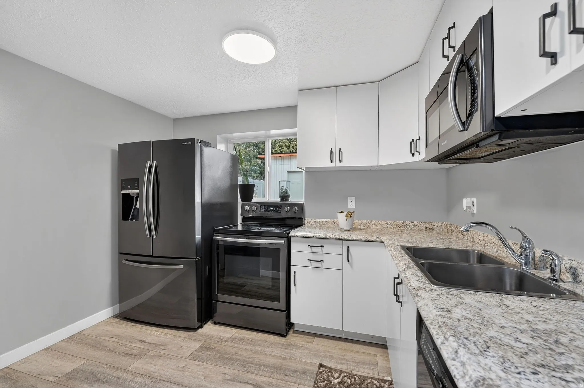 Kitchen featuring stainless steel range with electric cooktop, white cabinetry, light wood-style floors, a textured ceiling, and light stone countertops