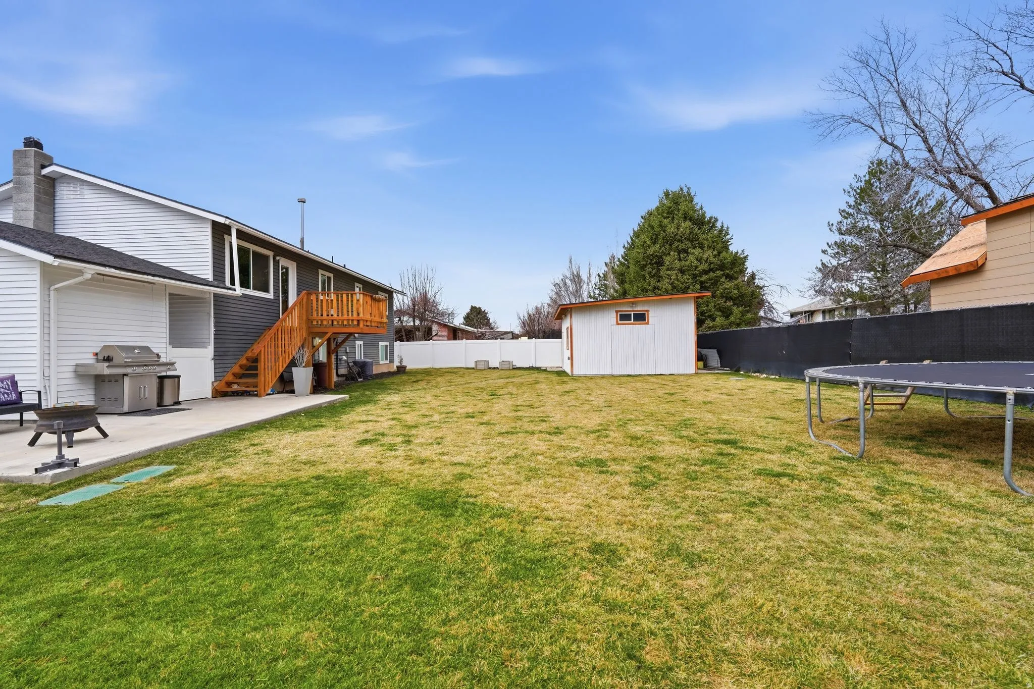 Fenced backyard featuring a patio, a trampoline, a storage shed, a wooden deck, and a fire pit