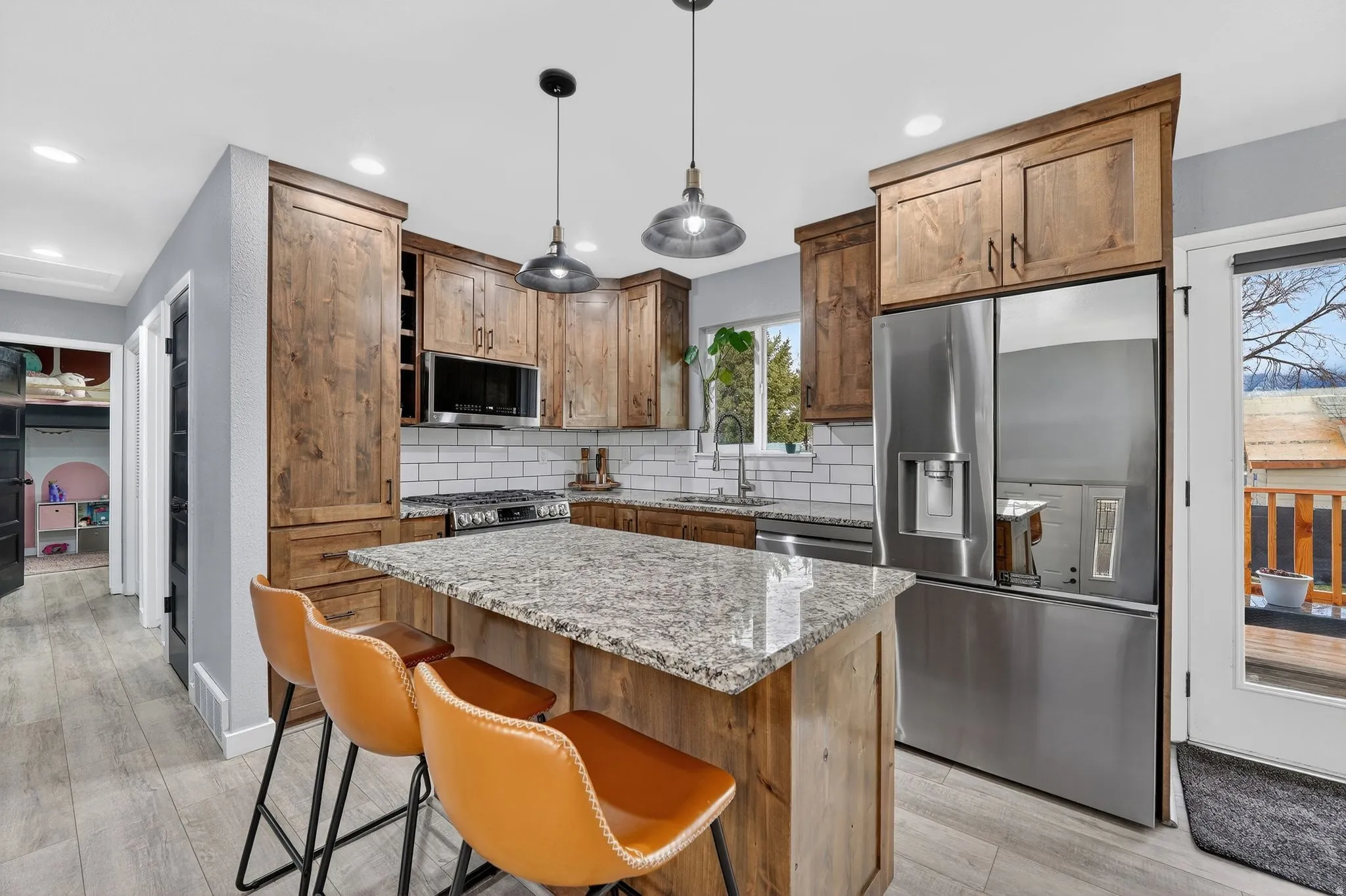 Kitchen with stainless steel appliances, light stone counters, a kitchen island, hanging light fixtures, and tasteful backsplash