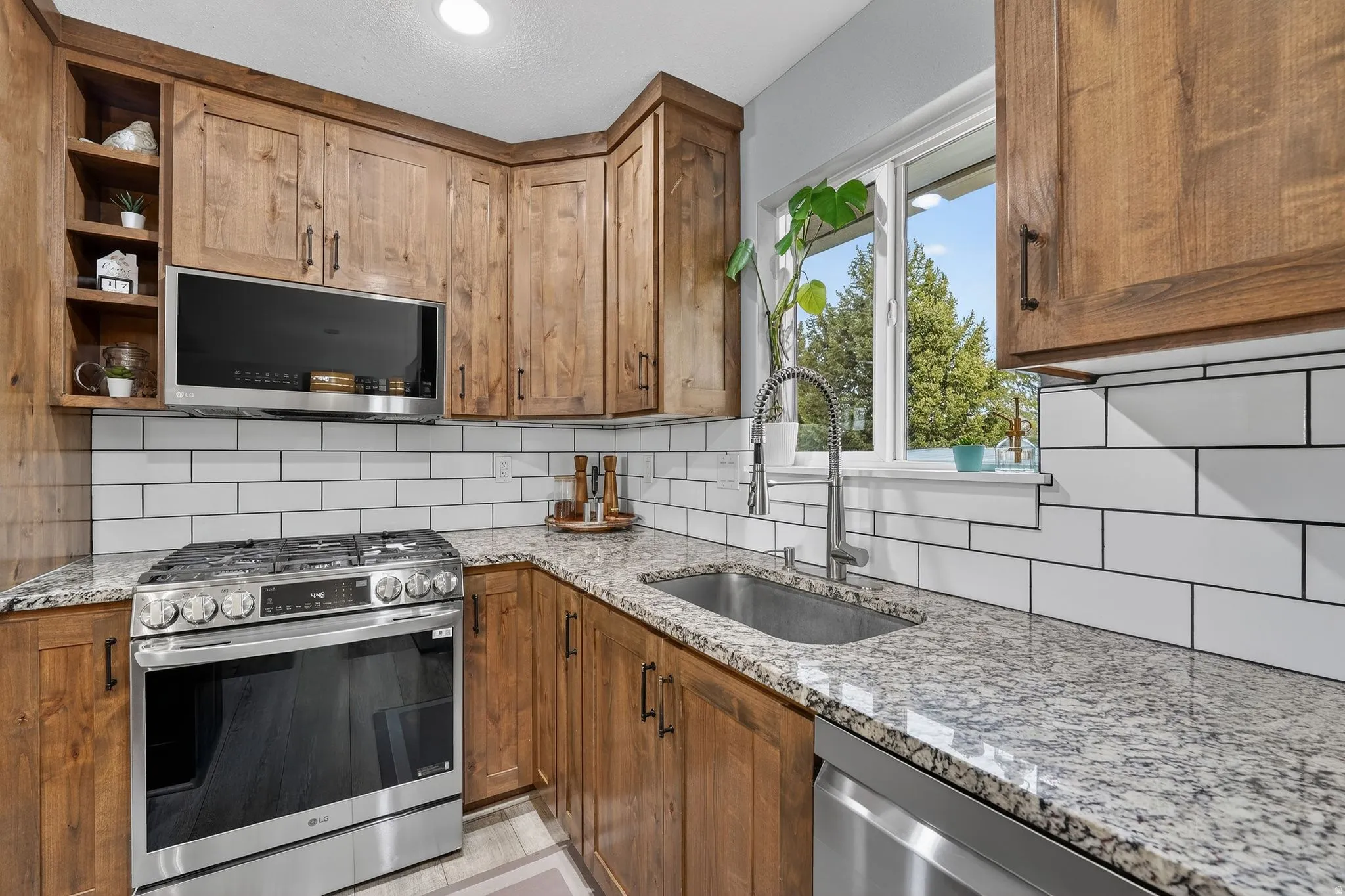 Kitchen featuring stainless steel appliances, light stone countertops, wood finish cabinetry, and decorative backsplash
