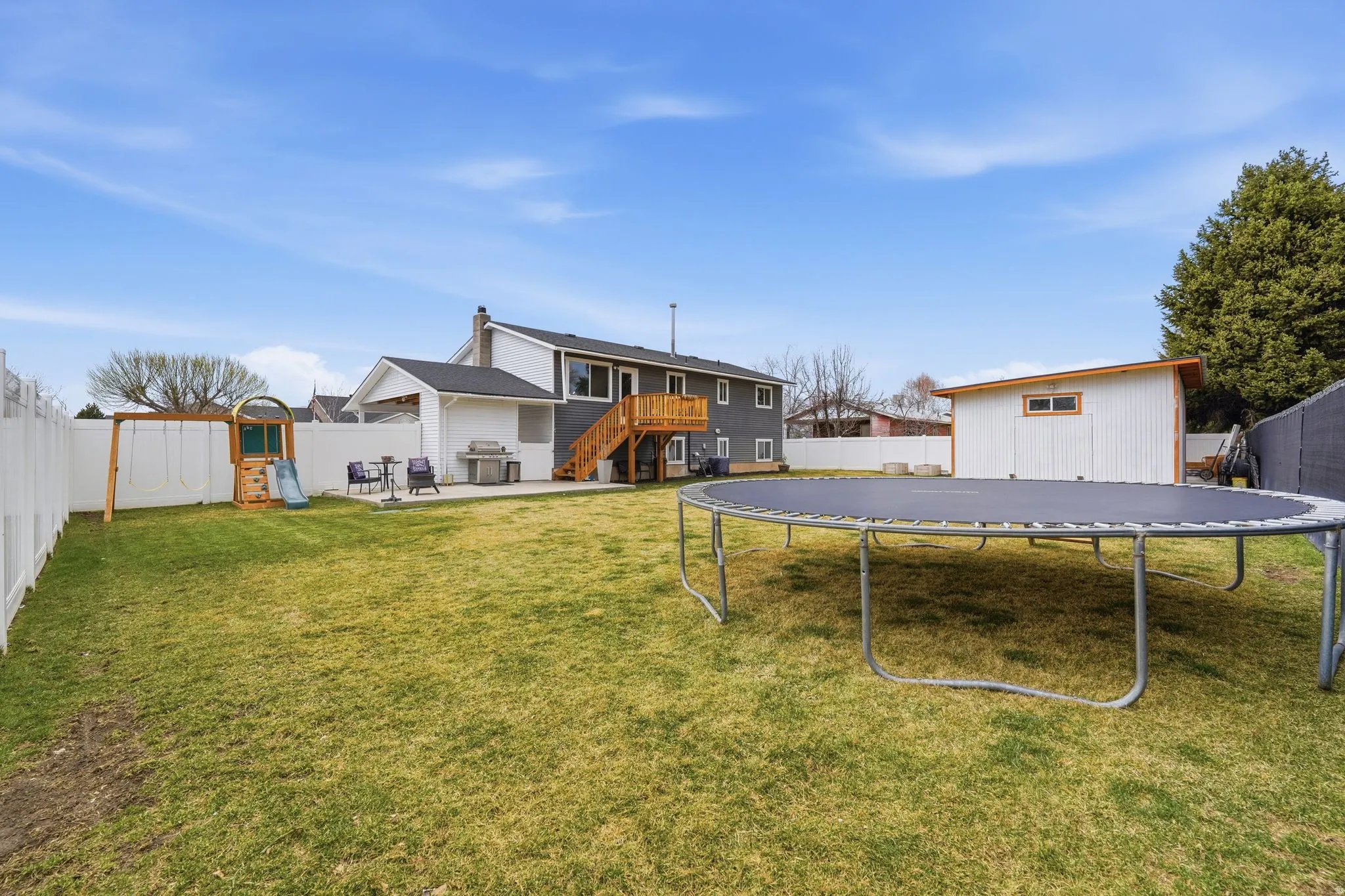 Rear view of house with a trampoline, a patio, a playground, and a fenced backyard