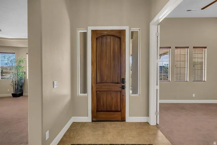 Foyer entrance with light carpet, light tile patterned flooring, and a ceiling fan