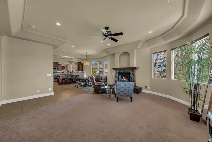 Living room with a raised ceiling, a ceiling fan, recessed lighting, carpet flooring, and a premium fireplace