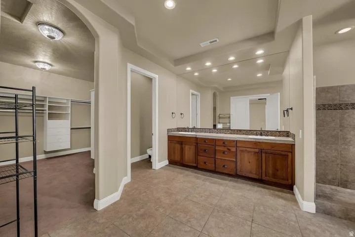 Bathroom with double vanity, walk in shower, a spacious closet, light tile patterned floors, and recessed lighting