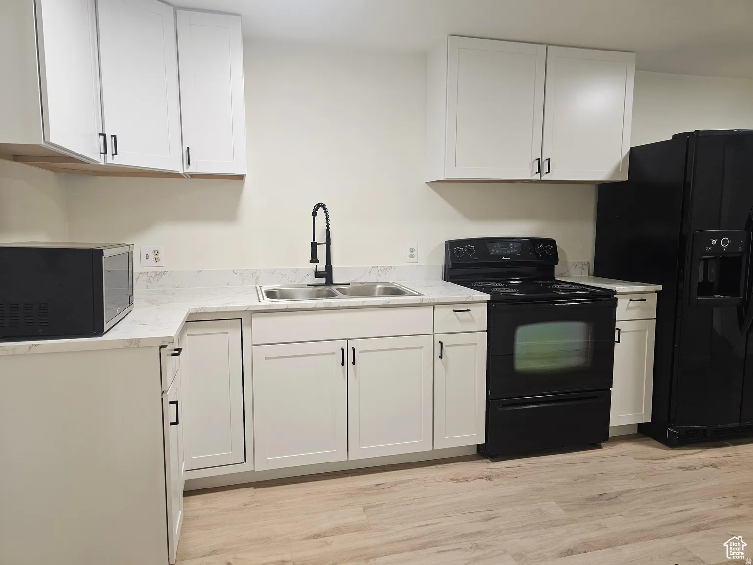 Kitchen with black appliances, white cabinets, light countertops, and light wood-style floors