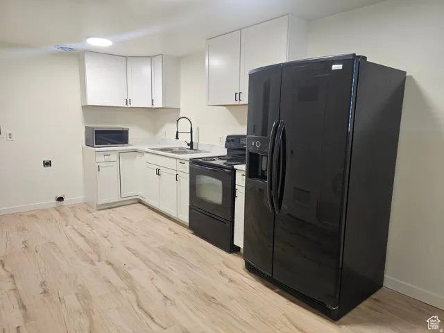 Kitchen featuring black appliances, white cabinets, light countertops, and light wood-style floors