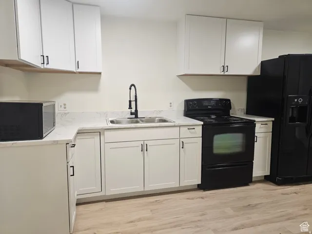 Kitchen with black appliances, white cabinets, light countertops, and light wood-style floors
