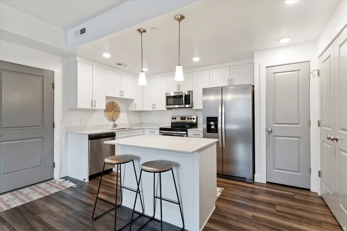 Kitchen featuring stainless steel appliances, a center island, white cabinets, and dark wood-style flooring