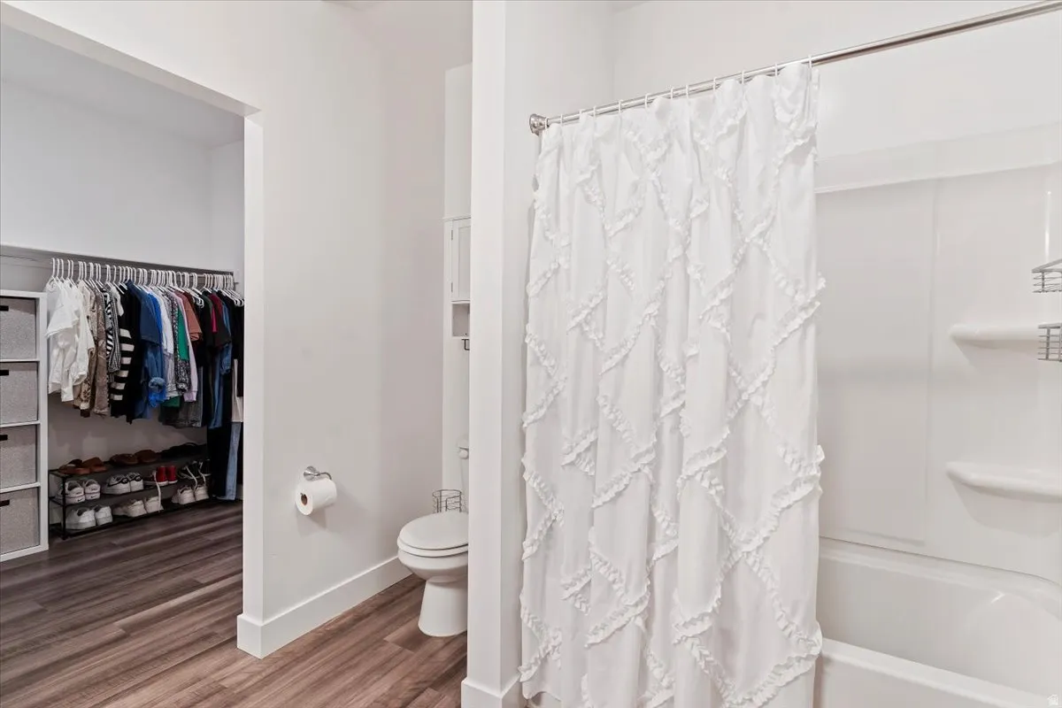 Full bath with wood finished floors, shower / bath combo with shower curtain, and a spacious closet