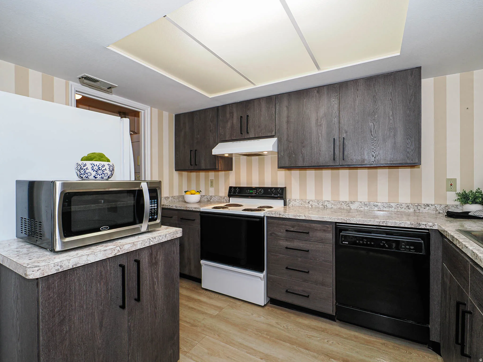 Kitchen with wallpapered walls, dark wood finish cabinets, electric range, black dishwasher, and light countertops