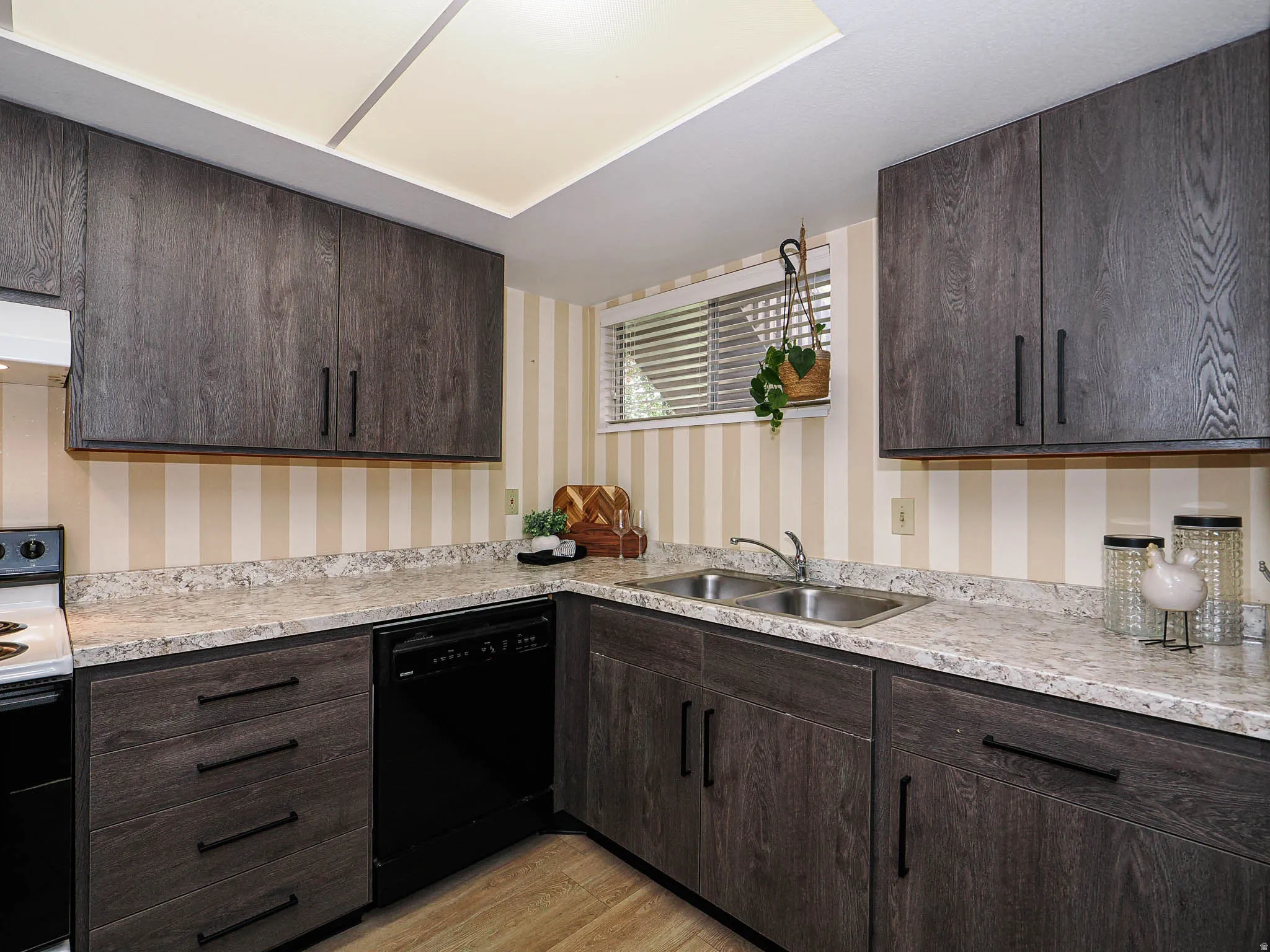 Kitchen featuring dark wood finish cabinets, electric range oven, dishwasher, and light wood-style flooring