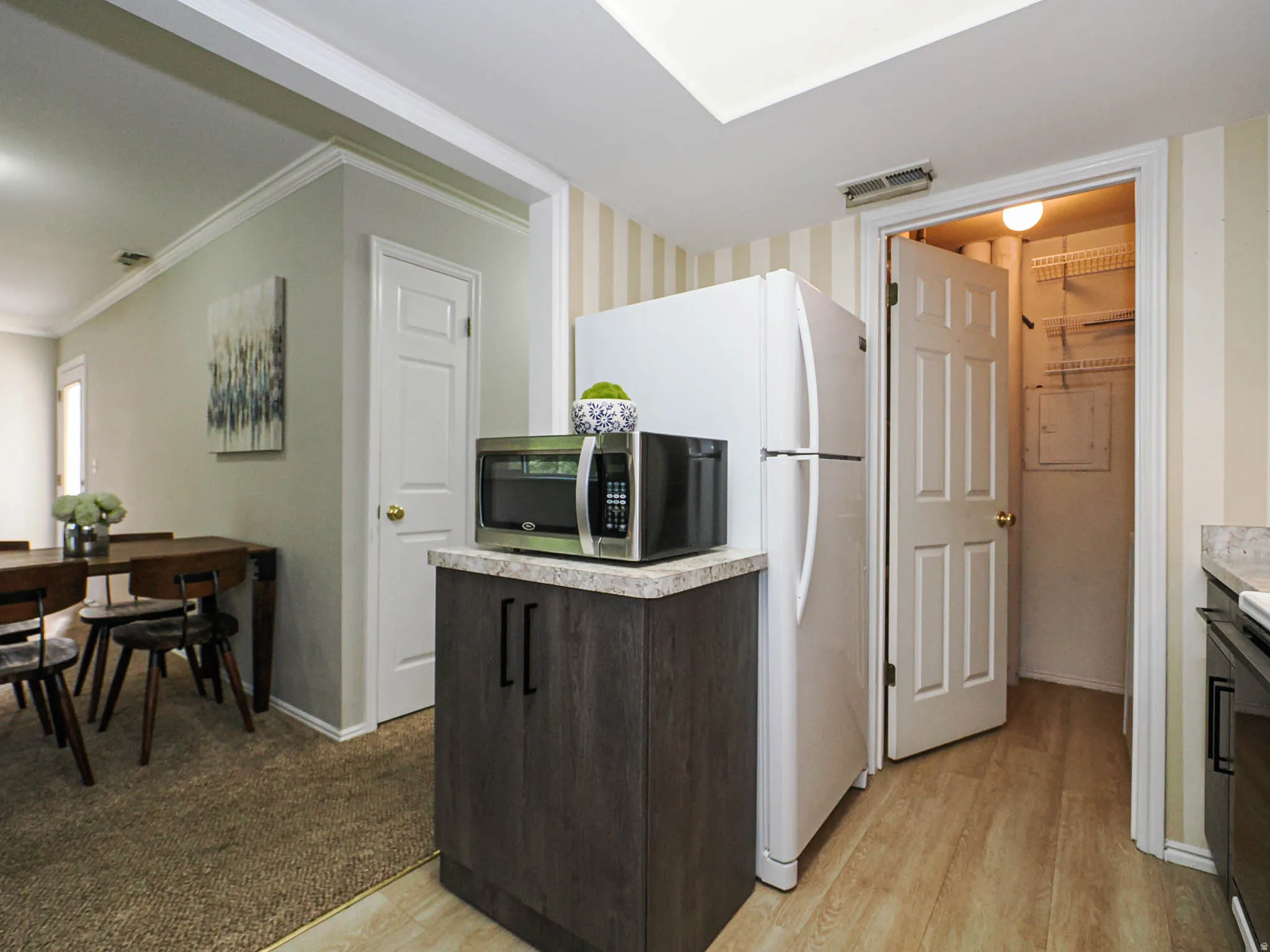 Kitchen with light countertops, stainless steel microwave, light wood-style floors, crown molding, and dark wood finish cabinets
