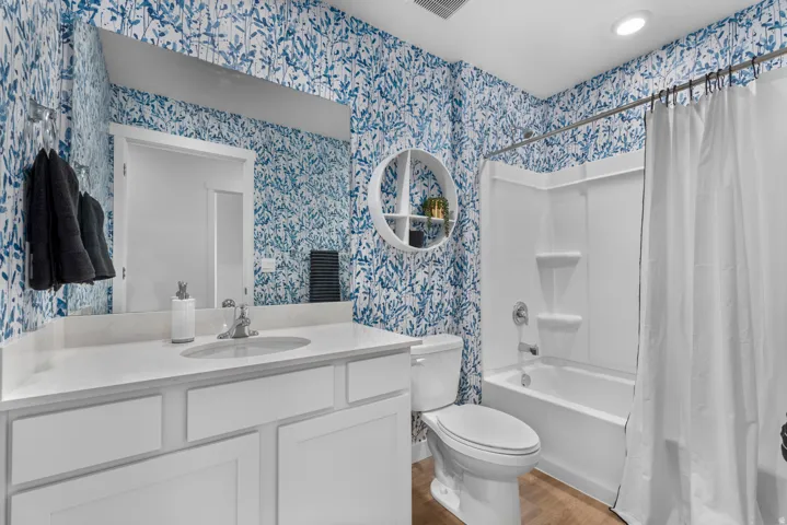Bathroom featuring vanity, shower / bathtub combination with curtain, light wood finished floors, and wallpapered walls