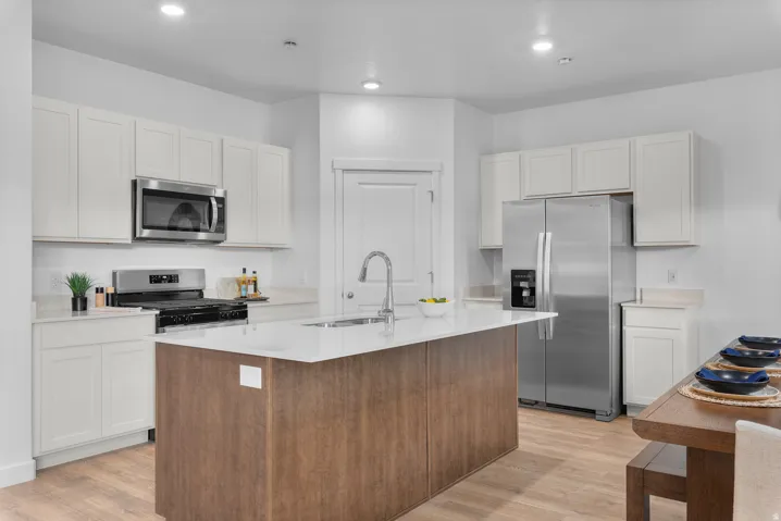 Kitchen with stainless steel appliances, an island with sink, light wood-type flooring, light stone counters, and recessed lighting