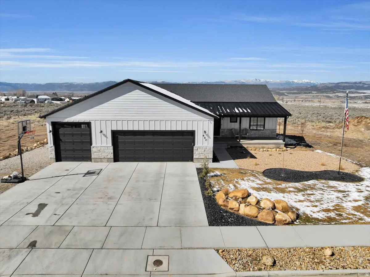 Modern farmhouse with stone siding, a mountain view, a porch, driveway, and a garage