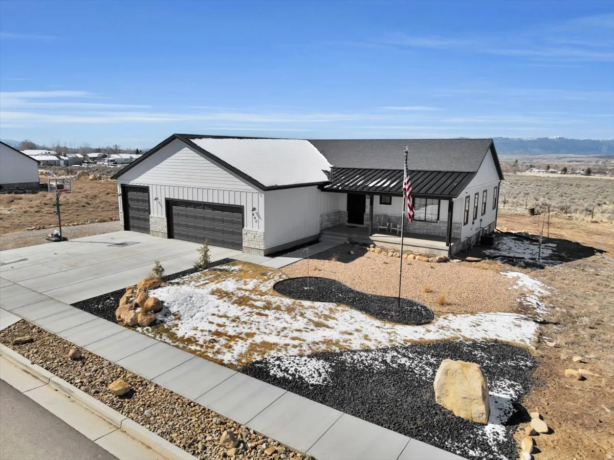 Modern inspired farmhouse featuring a standing seam roof, concrete driveway, a porch, stone siding, and a mountain view
