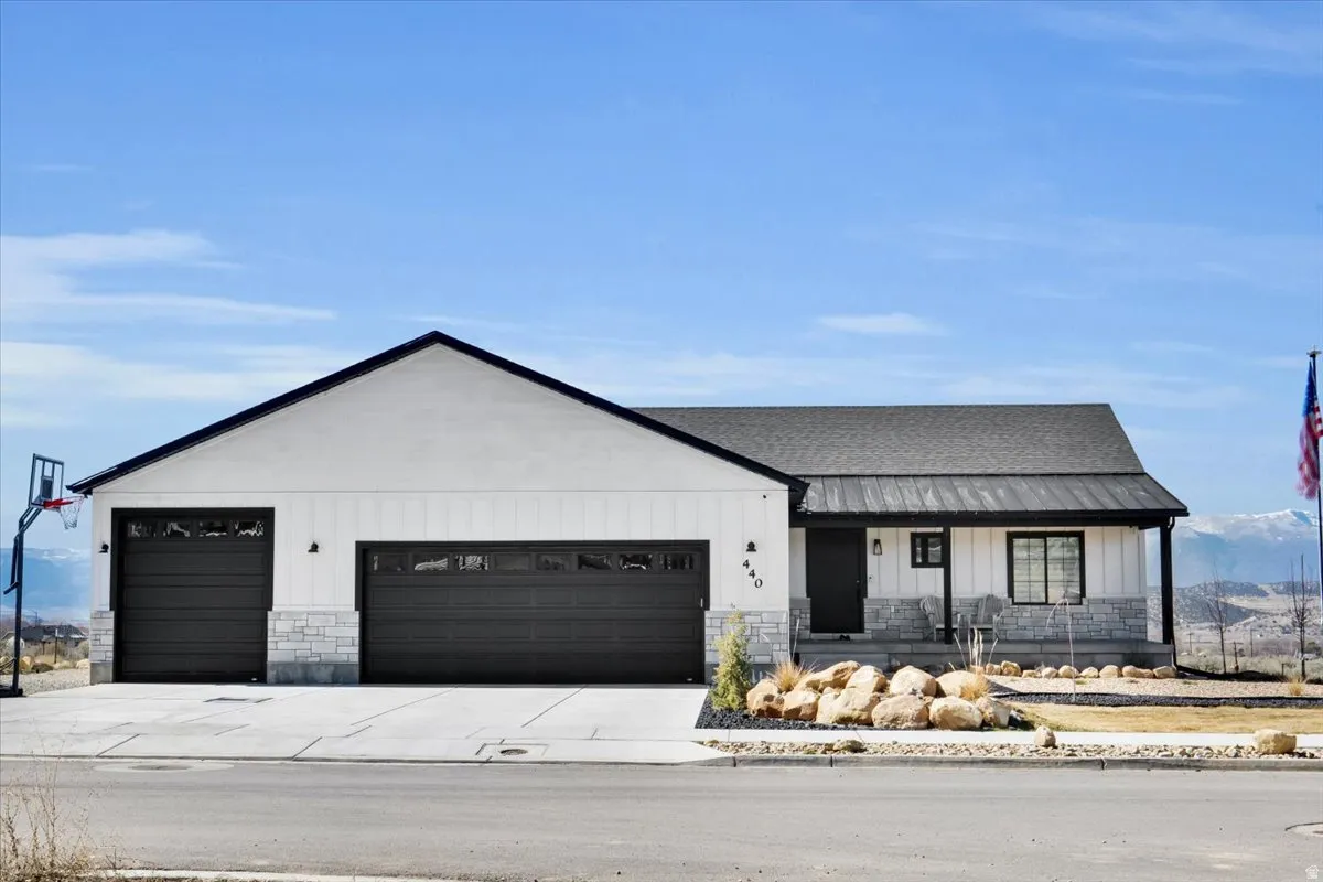 Modern farmhouse style home with stone siding, covered porch, board and batten siding, an attached garage, and a shingled roof
