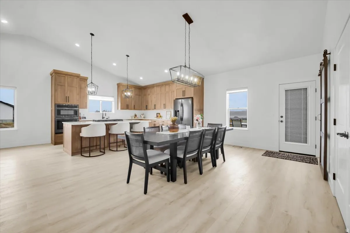 Dining space with a barn door, light wood-style flooring, vaulted ceiling, and hanging lights