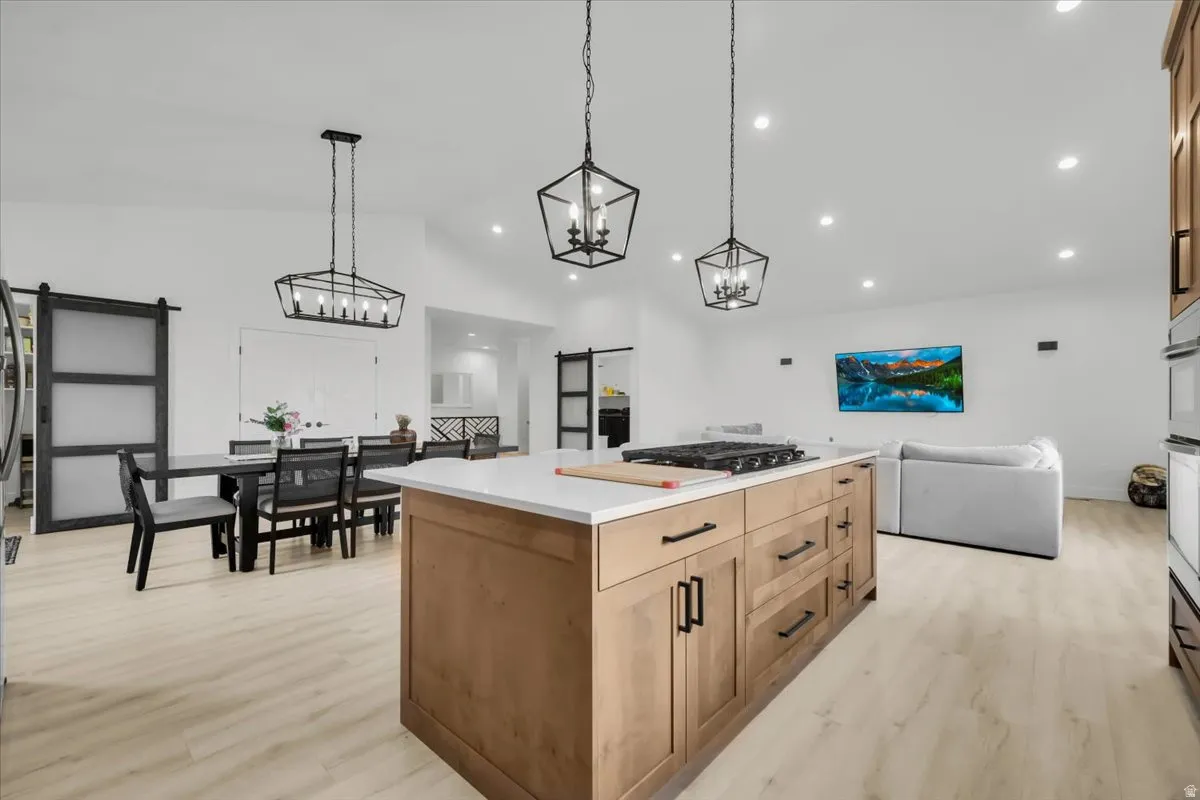 Kitchen featuring a barn door, light wood finished floors, a center island, open floor plan, and vaulted ceiling
