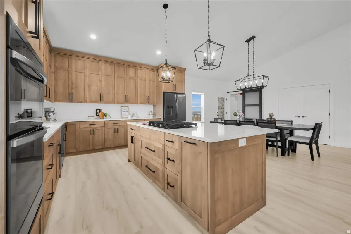 Kitchen with a kitchen island, double wall oven, light wood finished floors, light stone countertops, and stainless steel fridge