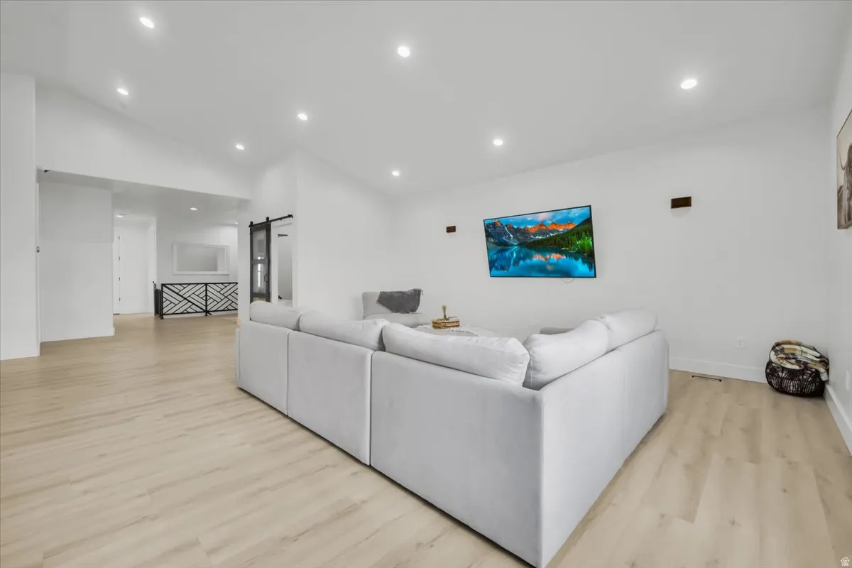 Living area with a barn door, light wood-style floors, recessed lighting, and vaulted ceiling