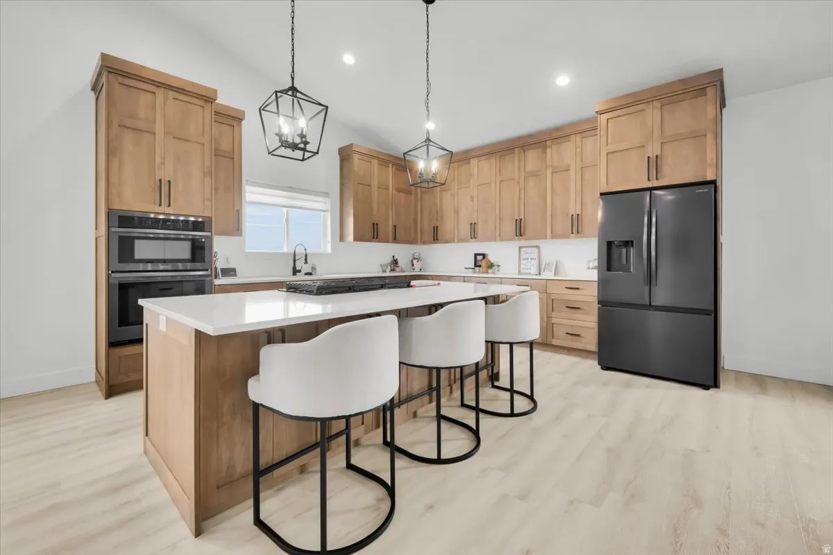 Kitchen with black fridge with ice dispenser, a center island, a breakfast bar, double oven, and light wood-style floors