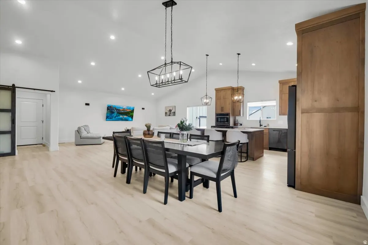 Dining area featuring a barn door, light wood-style flooring, hanging lights, and lofted ceiling