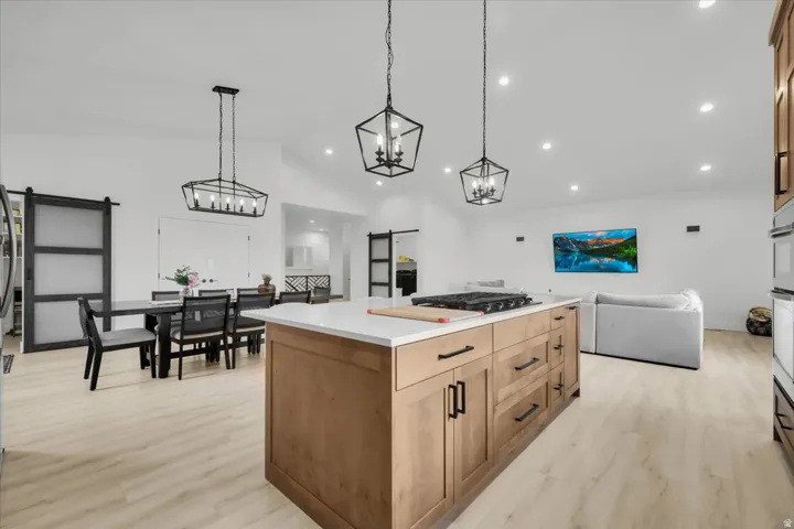 Kitchen featuring a barn door, light wood finished floors, a center island, open floor plan, and vaulted ceiling