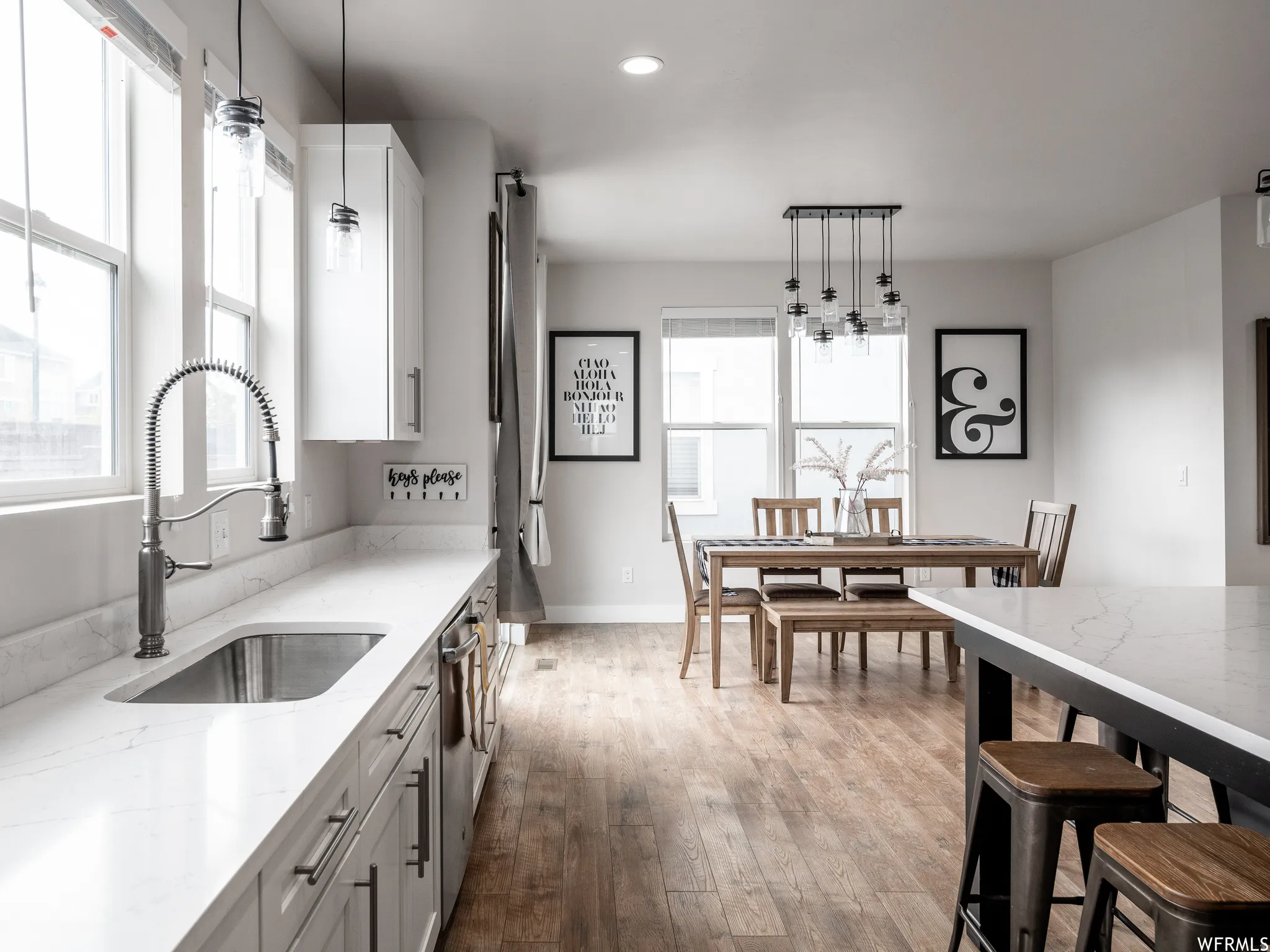 Kitchen with light stone countertops, light wood finished floors, pendant lighting, stainless steel dishwasher, and white cabinets