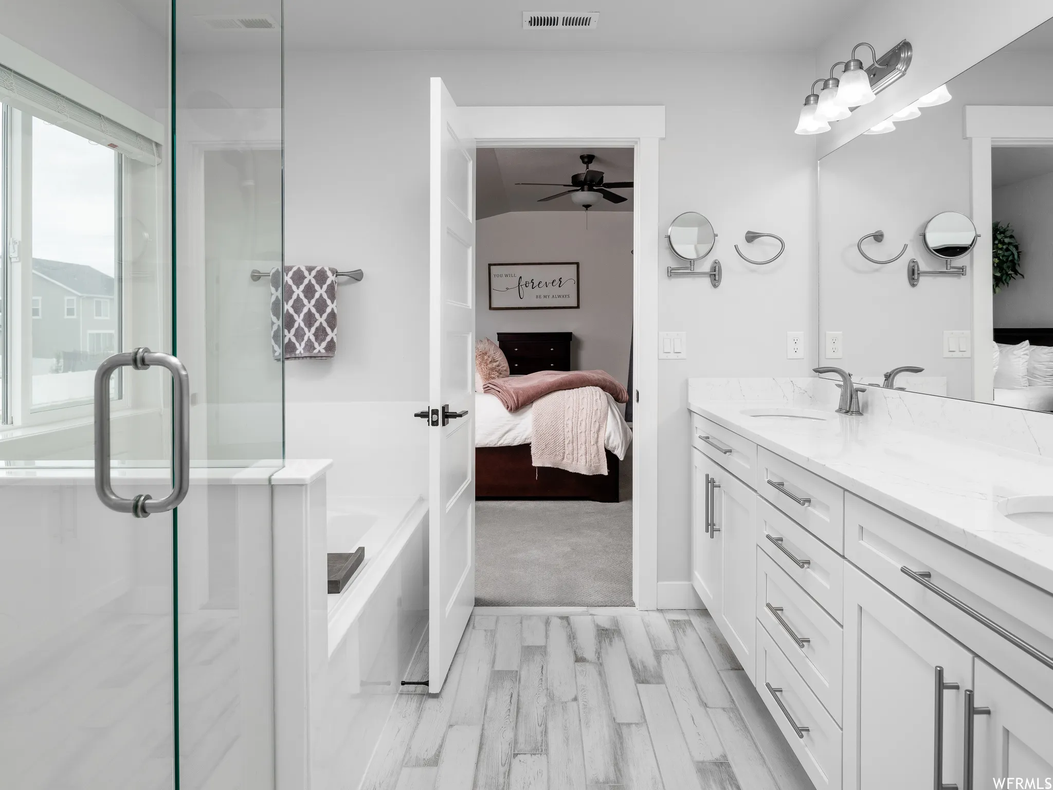 Ensuite bathroom featuring double vanity, a bath, a shower stall, light wood-type flooring, and ceiling fan